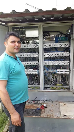 Açık duran elektrik panosunun yanında duran elektrik ustası; sıralı otomat sigortalar ve klemens bağlantıları görünüyor